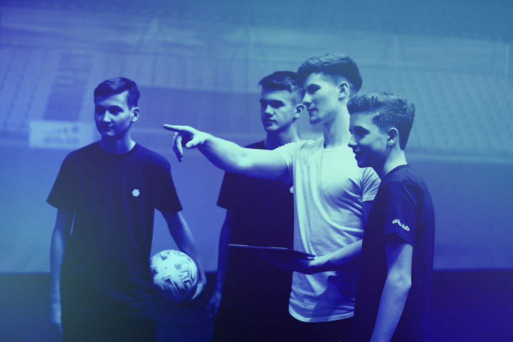 A skills.lab coach giving instructions to three youth players during an open training